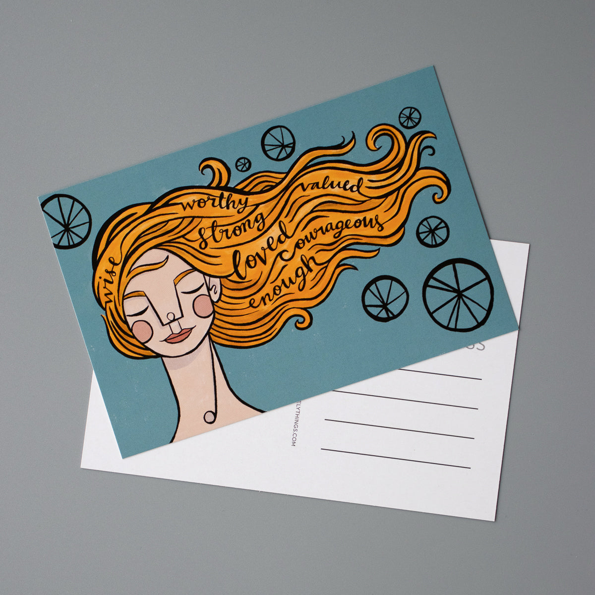 Postcards with the illustration of a woman with orange hair blowing in the wind. In her hair are the words: wise, worthy, strong, valued, loved, courageous, and enough.