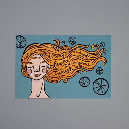 Front of the Identity postcard: A woman with orange hair on a blue background. Encouraging words are in her hair that blows in the wind.